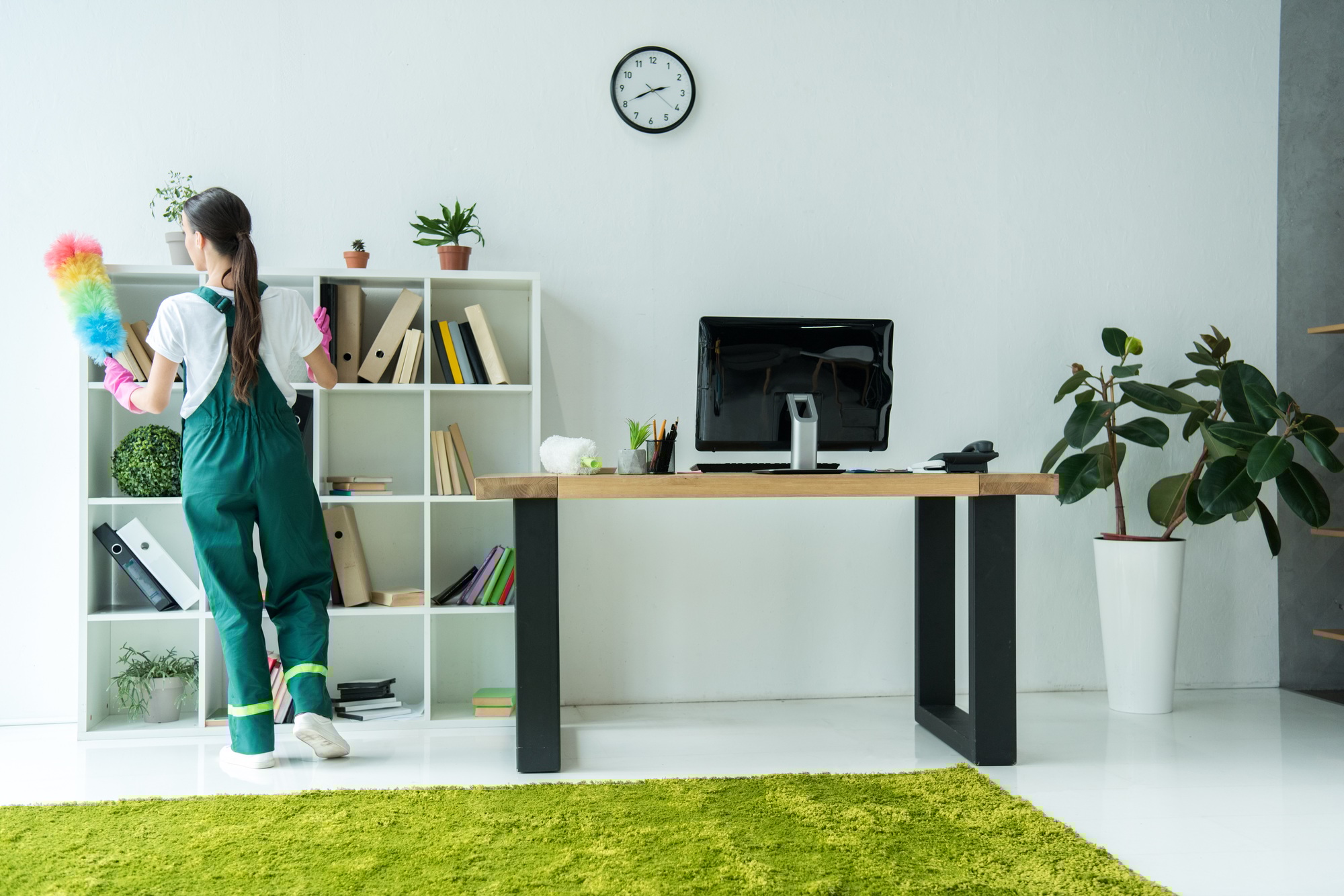 back view of young cleaner holding duster and cleaning modern office
