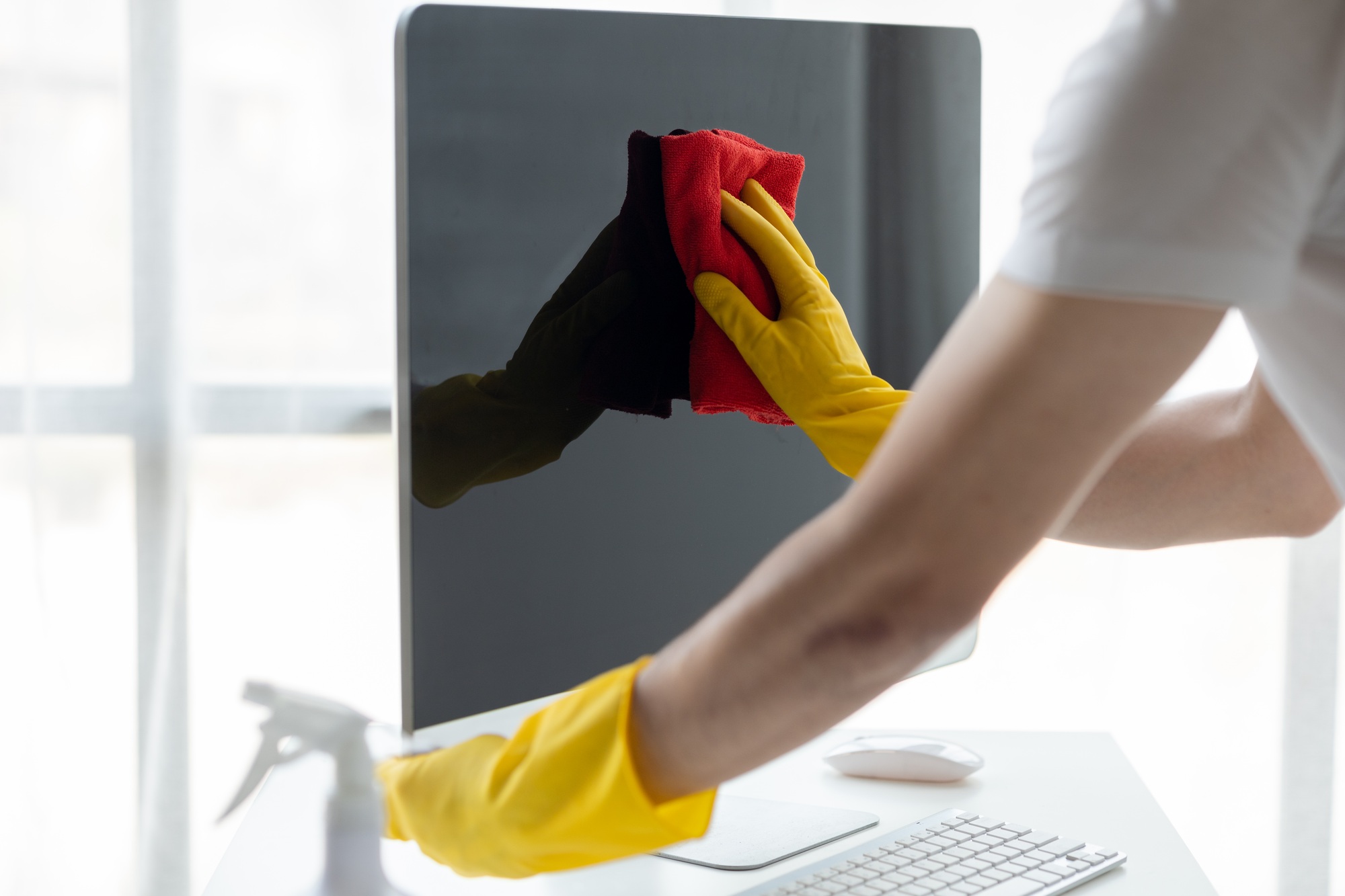 Person cleaning room, cleaning worker is using cloth to wipe computer screen in company office room.